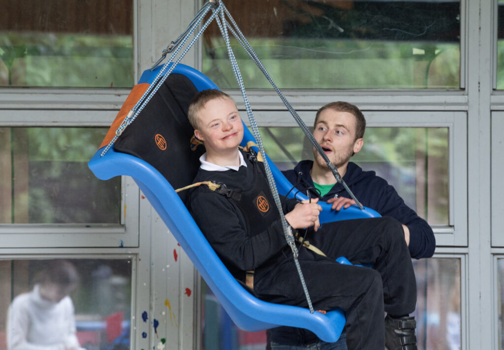 Little boy using the sensory swing, being pushed by a member of Yard staff