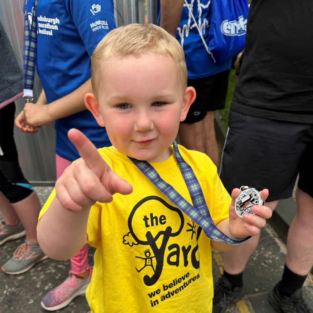 Little boy in yellow Yard t-shirt with his medal after completing a challenge event.