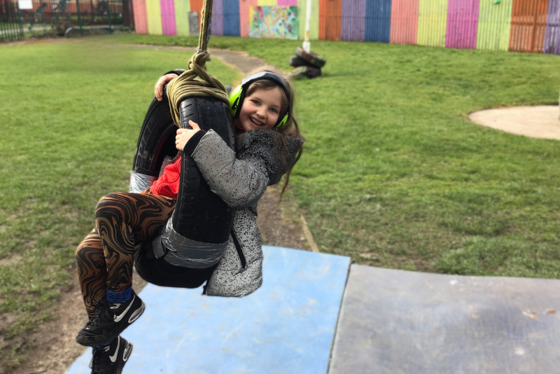 Young girl wearing ear defenders on the tyre swing at The Yard Dundee.