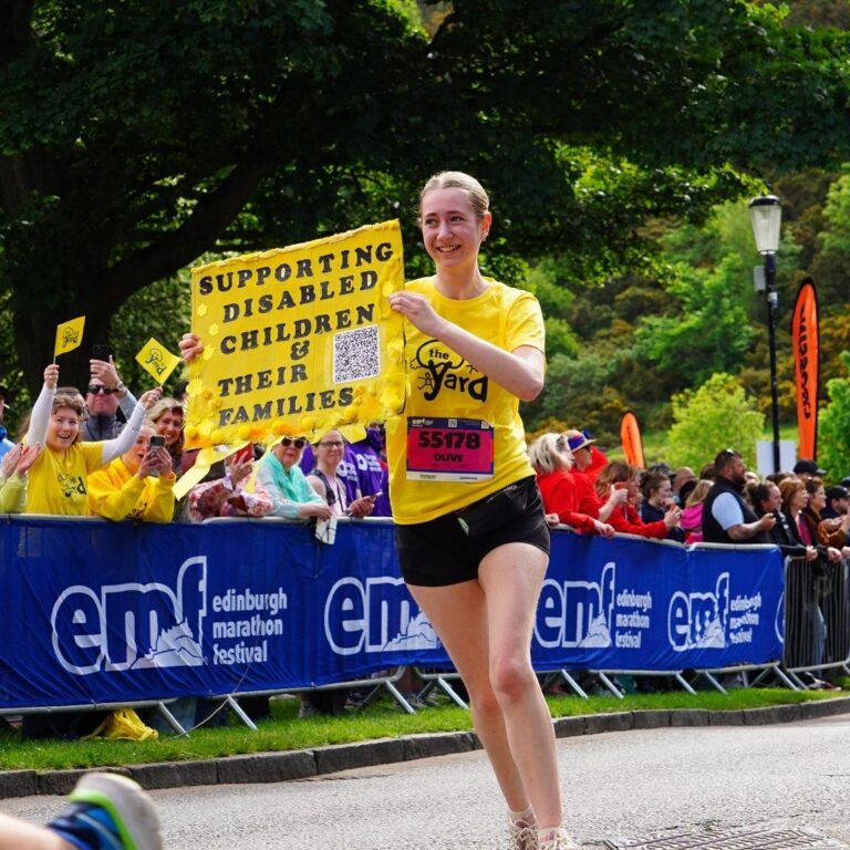 Marathon runner wearing Yard tshirt and holding up sign that says 'Supporting disabled children and their families'